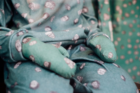 A detail of a figures hand and green and patterned upholstered form in the installation.