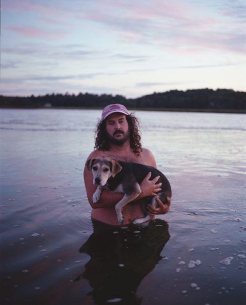 It's Colby! He's waist-deep in the ocean and holding his dog Tina. It's a beautifully Maine picture and weirdly intimate. Colby is wearing a hat. It seems to be near dusk. A light sunset cascades across the water. What a day.