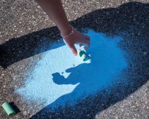 A photograph of powdered blue chalk on the ground and a hand reaching down to grab the little bit left of the chalk stick.