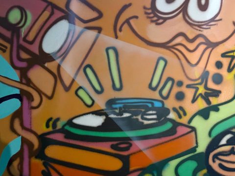 Mural detail of a spray painted image of a Hollywood-type spotlight focusing on a record player.