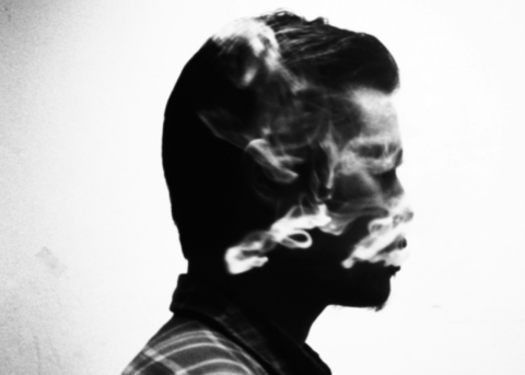 A black and white photographic double exposure of a man in silhouette with white smoke over his face