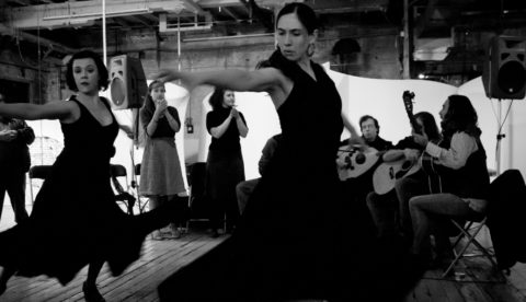 A black and white photo of flamenco dancers with a band in silhouette in the background