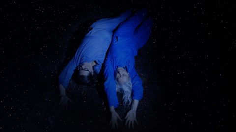 Two women sliding backwards, wearing blue jumpsuits