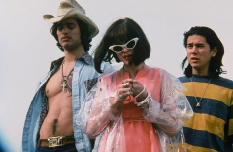 3 main characters standing- one in a cowboy hat, one wearing sunglasses, one in stripes