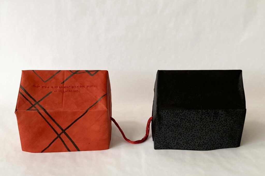 An image of a red and black house sculpture with thread connecting them.