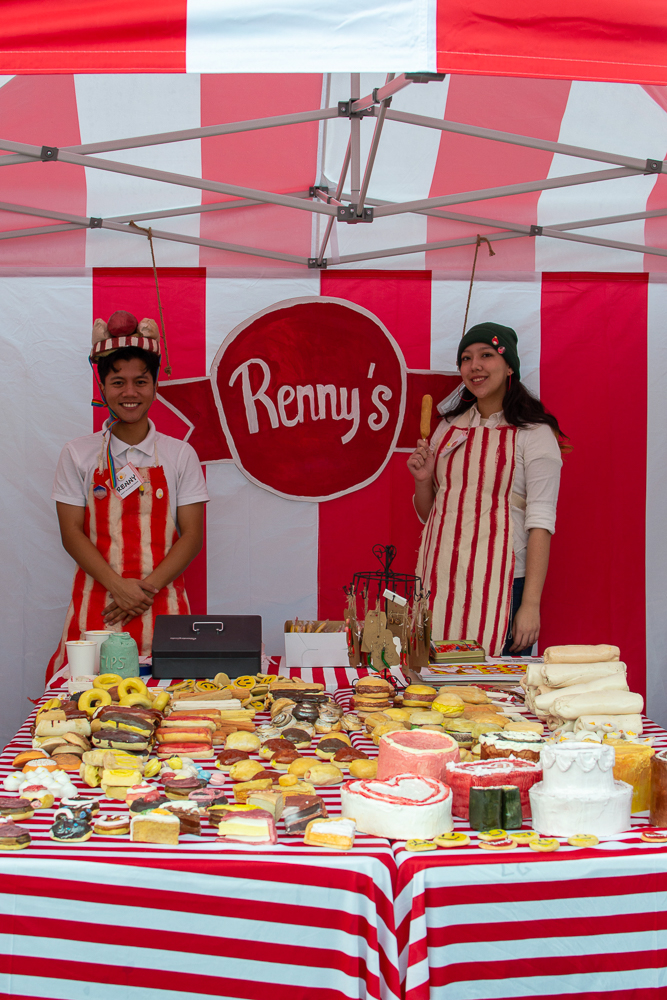 Two individuals in red and white striped aprons stand in a red and white striped ceramics vendor tent