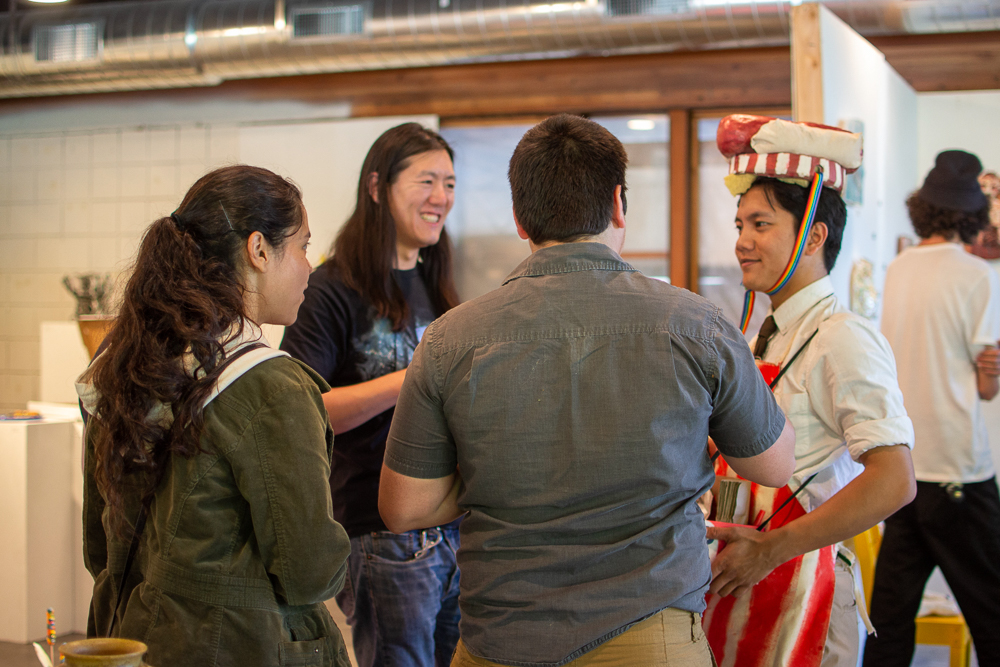 man in striped apron and ceramic hot dog hat approaching three people