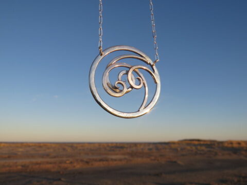 Photograph of a silver necklace pendant with a landscape in the background