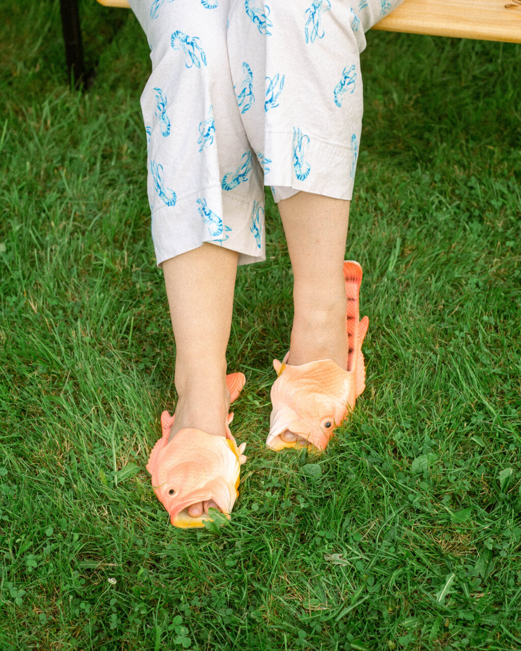 a person shows their shoes with metallic orange fish sandles under the grass