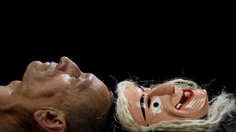 a staged image of the face of an older man and a mask lying side by side against a black background