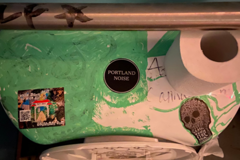 A top down photograph of the back of a toilet in a club, with a Portland Noise sticker