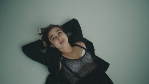 A still from the film Apolonia of a girl laying with her head wresting on her arms looking up.