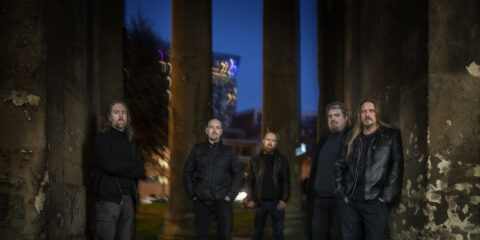 Esoteric at dusk looking metal as all hell, standing expressionless in front of columns, a blurred city scape behind them. They're wearing all black of course.