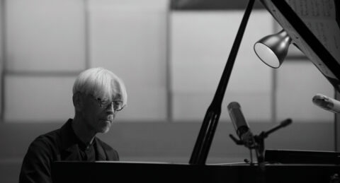 The composer Ryuichi Sakamoto sits at a piano