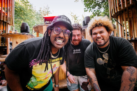 The three members of the Philadelphia hardcore band Soul Glo huddle outside while smiling at the camera