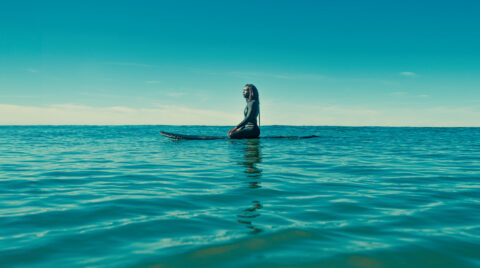 Surfer Sierra Raequel sits on a surfboard in a great expanse of ocean water in this film still