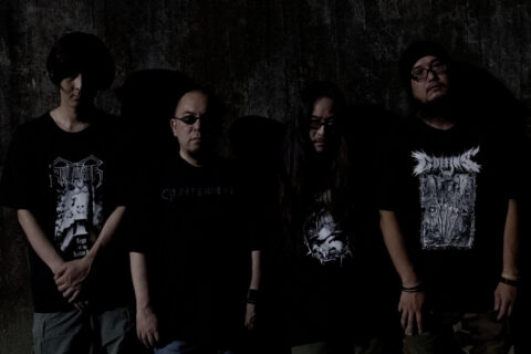 The four members of the Japanese band Coffins wear black punk/metal clothes against a darklit black background