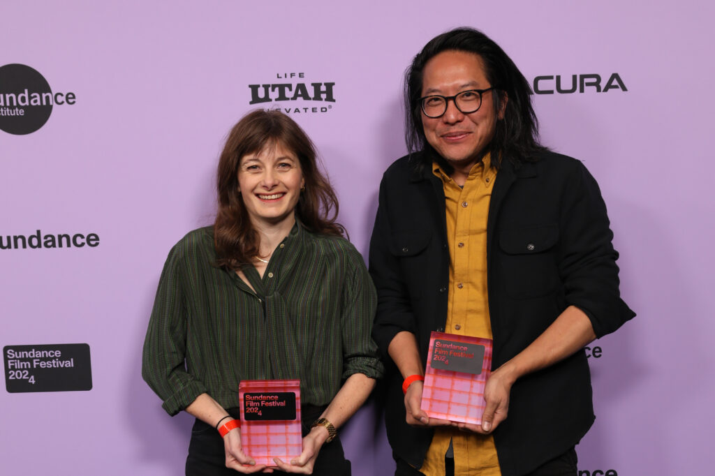 Two figures holding pink awards against a pink backdrop. 