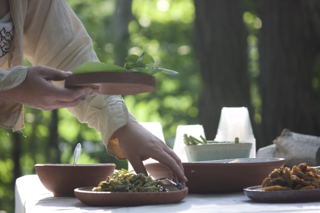 A hand passing food on a handmade plate (made from former brick material from the site) at Rachel Alexandrou's Re-Site meal. 