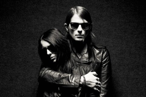 Wes Eisold and Amy Lee of Cold Cave stand entwined in a black backdrop