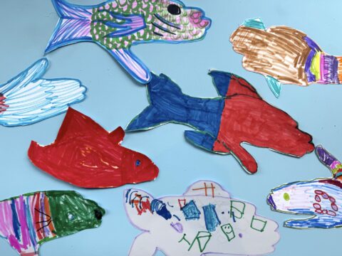 A photograph of young student art making a school of fish, each traced from a students hand and colored in with various colored markers.