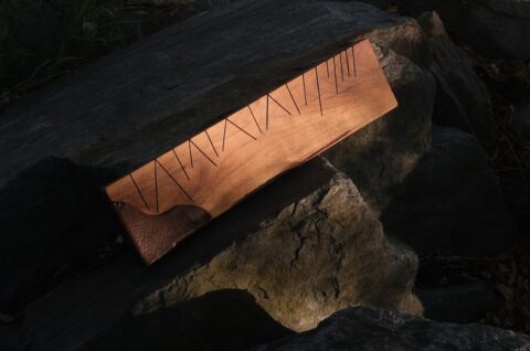 A dark image of a handmade wood instrument with various geometric black lines crossing the wood surface.
